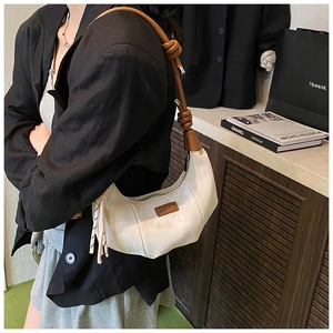 Detail view of white crescent bag with brown leather knotted strap and logo tag