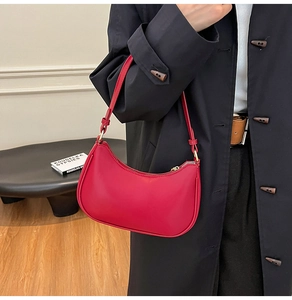 Modern red leather half-moon shoulder bag styled with a black coat in a chic studio