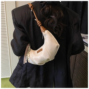 Detail of a creamy half-moon bag with brown knot strap shown against a black blazer background