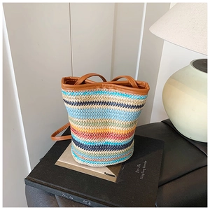 Close-up of rainbow striped straw bucket bag with brown faux leather trim and handle