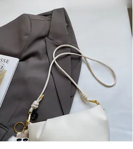 Close-up of white leather dumpling bag with knotted strap and plush eye charm detail