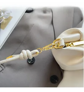 Close-up of golden metal clasp and white leather strap with decorative knot detail