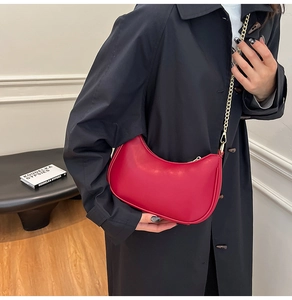 Red leather crescent shoulder bag with gold chain strap shown on a black coat outfit