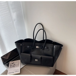 Close-up of a large black leather tote bag featuring triple front pockets and metal buckles