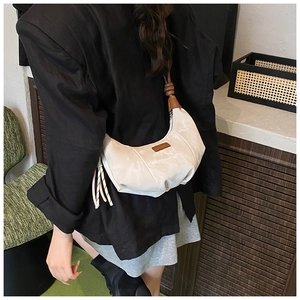 Detail of off-white pleated dumpling bag with brown leather tag and woven charm