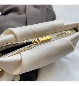 Close-up of smooth golden zipper and lychee grain texture on off-white crossbody bag