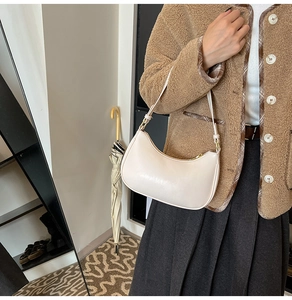 Detail view of a beige leather half-moon hobo bag on shoulder with gold hardware