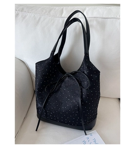 Close-up of black polka dot tote bag with bow detail and leather trim on a sofa