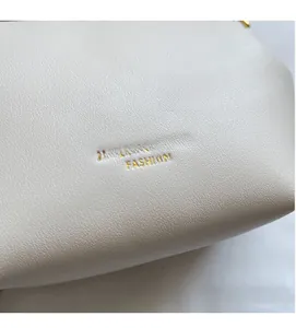 Detail of off-white lychee grain leather texture with gold lettering on stylish crossbody bag
