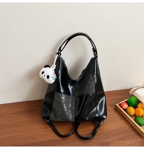Détail du sac hobo noir brillant avec un pendentif panda en peluche et panneaux texturés