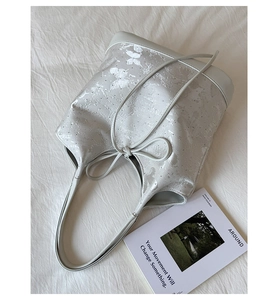 Close-up of a stylish silver bucket bag with butterfly patterns and drawstring bow detail