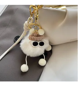 Detail of plush white ball bag charm with brown knit hat and sunglasses on handbag