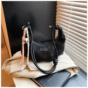 Detail of black crescent hobo bag with knotted strap and silver heart charm on a blazer