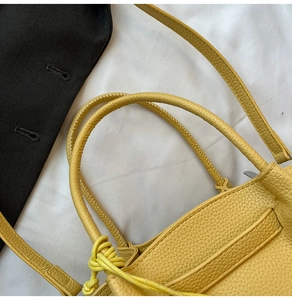 Detailed close-up of yellow pebbled leather bucket bag with top handles and decorative knot