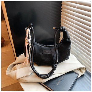 Detail of black crescent bag with knotted strap and metal heart pendant decoration