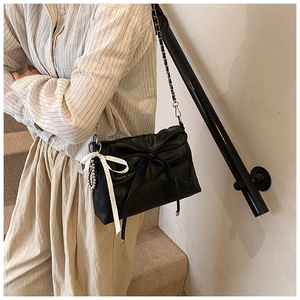 Detail of black crossbody bag featuring bow stitching and a white satin ribbon charm