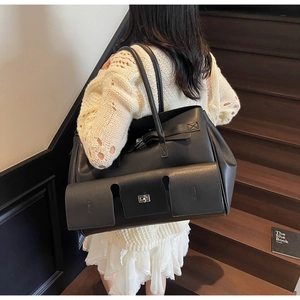 Close-up of black leather tote bag with silver rotary lock shown on model indoors