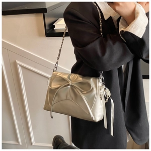 Detail of silver metallic ballet-style crossbody bag with bow and pearl chain on a model