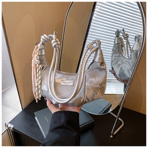 Close-up of silver satin crescent bag with knotted handles and tassel charm detail