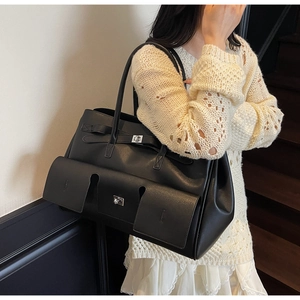 Detail of black leather tote bag featuring dual front pockets with silver twist-lock closures