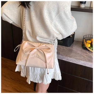 Close-up of cream bow shoulder bag with silver chain strap shown in a lifestyle setting