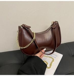 Close-up of a dark brown crescent-shaped shoulder bag with gold metal chain and leather strap