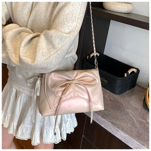 Close-up of pearl pink crossbody bag with bow detail and silver chain strap on model