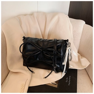 Detail of black pleated cloud bag with oversized bow and silver chain on a beige blazer