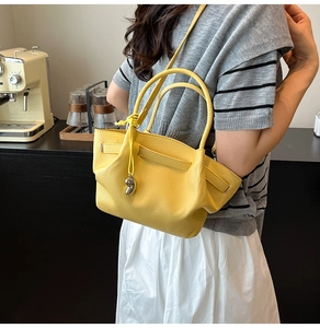 Detail of bright yellow lychee textured leather bucket bag with silver charm in a cafe