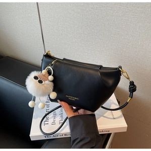 Détail du sac dumpling noir minimaliste avec logo doré et charm de poupée en peluche blanche