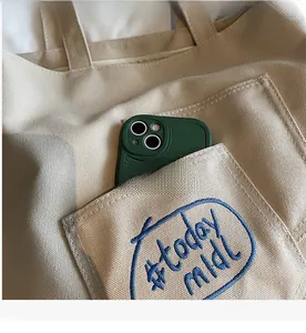 Close-up of beige canvas tote bag front pocket with #today mood embroidery and green phone
