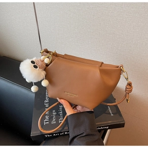 Sac à main géométrique marron avec breloque pelucheuse blanche porté à la main