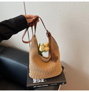 Detail of woven straw tote bag with brown leather strap, tassel and hollowed patterns