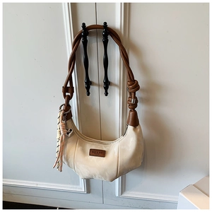 Close-up of pleated beige dumpling bag with woven strap and metal heart charm