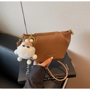 Détail d'un sac à bandoulière en cuir marron avec un porte-clé monstre en peluche