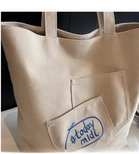 Close-up of durable beige canvas tote with blue Today Midi embroidery and functional front pocket