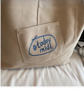 Detailed view of beige canvas tote bag featuring navy blue #today midi embroidery