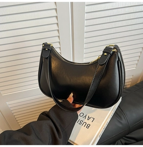 Detailed shot of a black minimalist leather crescent bag featuring gold metal zipper hardware