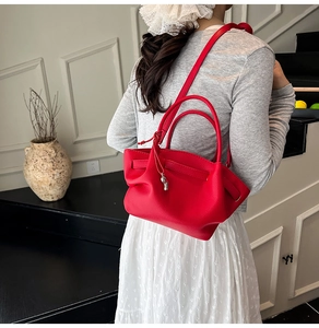 Model wearing a vibrant red lychee grain leather bucket bag with top handle and shoulder strap