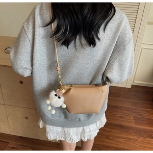 Détail du sac bandoulière beige avec logo doré et porte-clés monstre en peluche blanc