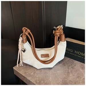 Detail of white half-moon bag featuring a brown knotted handle and heart-shaped pendant