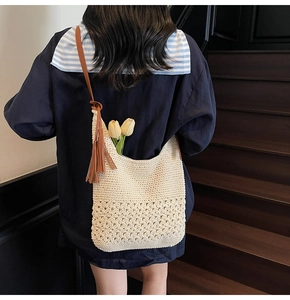 Detail of hollow woven beige hobo bag with brown leather strap and tassel decoration
