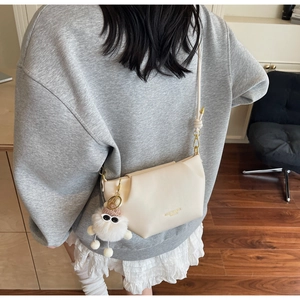 Détail du sac bandoulière plissé crème avec breloque en peluche porté par un mannequin