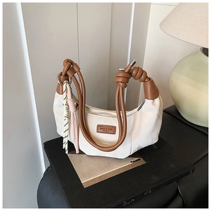 Detail of cream crescent bag with knotted brown leather handle and woven charm