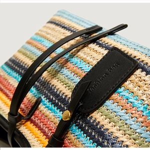 Detail of colorful woven bohemian bag with black leather logo tag and gold metal rivets