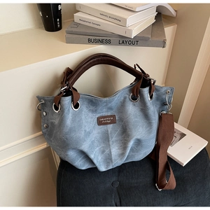 Detail of blue tote bag with brown leather handles and side metal eyelets on soft seat