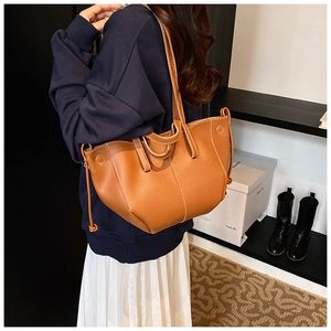 Detail of brown leather tote bag showing white decorative stitching and long slim straps