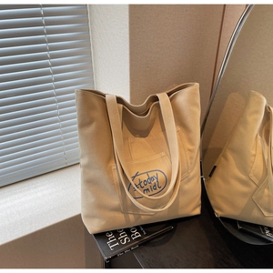 Close-up of beige canvas tote bag featuring blue 'today midi' embroidery and outer pocket