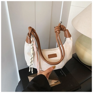 Close-up of beige dumpling bag with brown leather knotted handle and brand tag detail