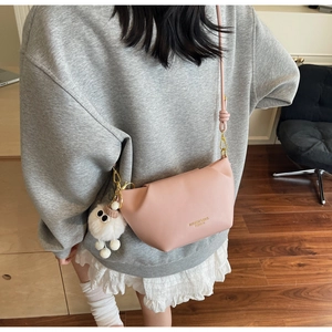 Détail du sac bandoulière rose clair avec logo doré et pendentif en peluche mignon
